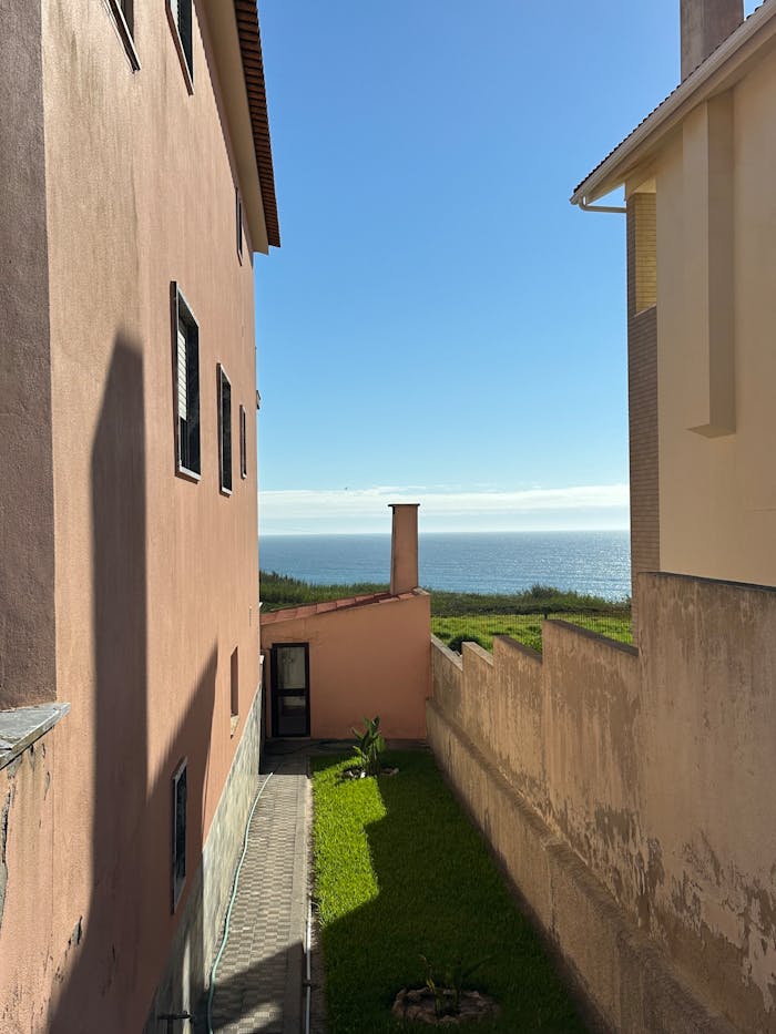 Coastal view between buildings in A dos Cunhados, Portugal. Clear day, ocean in the background.