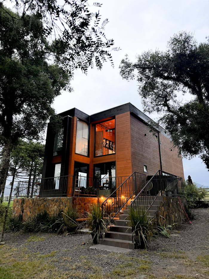 A contemporary wooden cabin with warm lighting nestled among trees, creating a cozy outdoor atmosphere.